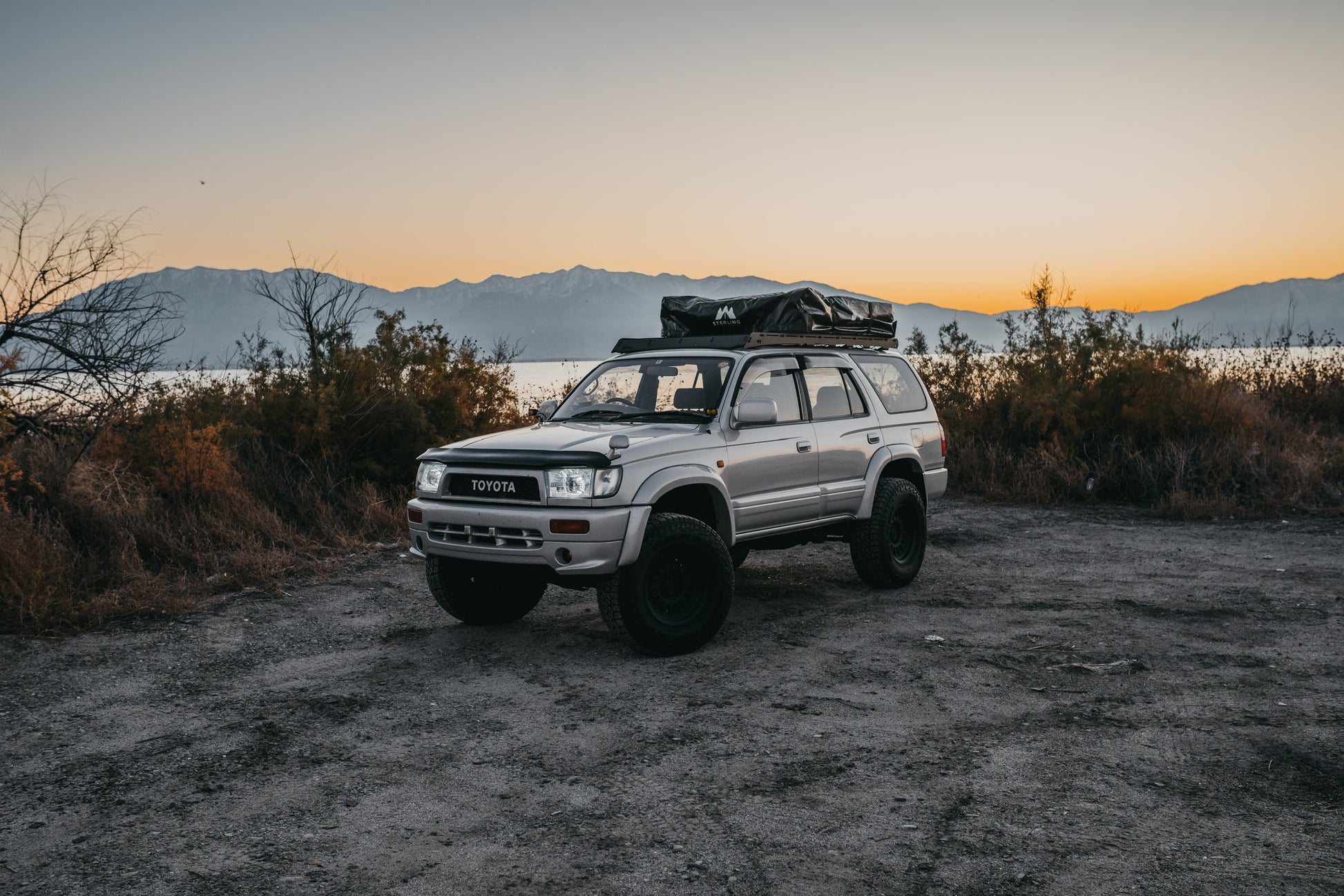 Closed Soft Shell rooftop tent on a Hilux Surf, parked at a lake with a sunrise